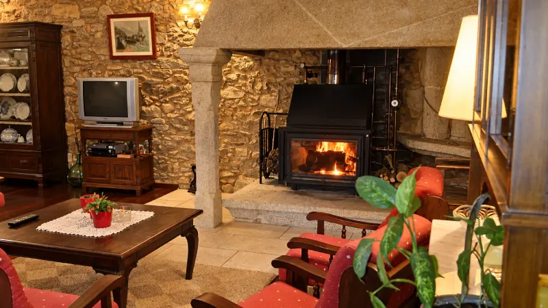 Chimenea encendida en el salón común del hotel rural Casa do Vento, con paredes de piedra y sillones.