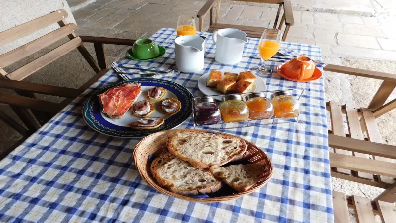 Desayuno servido en Casa do Vento, con pan, tostadas con jamón, mermeladas, bizcocho y zumo de naranja recién exprimido en la terraza del hotel rural.