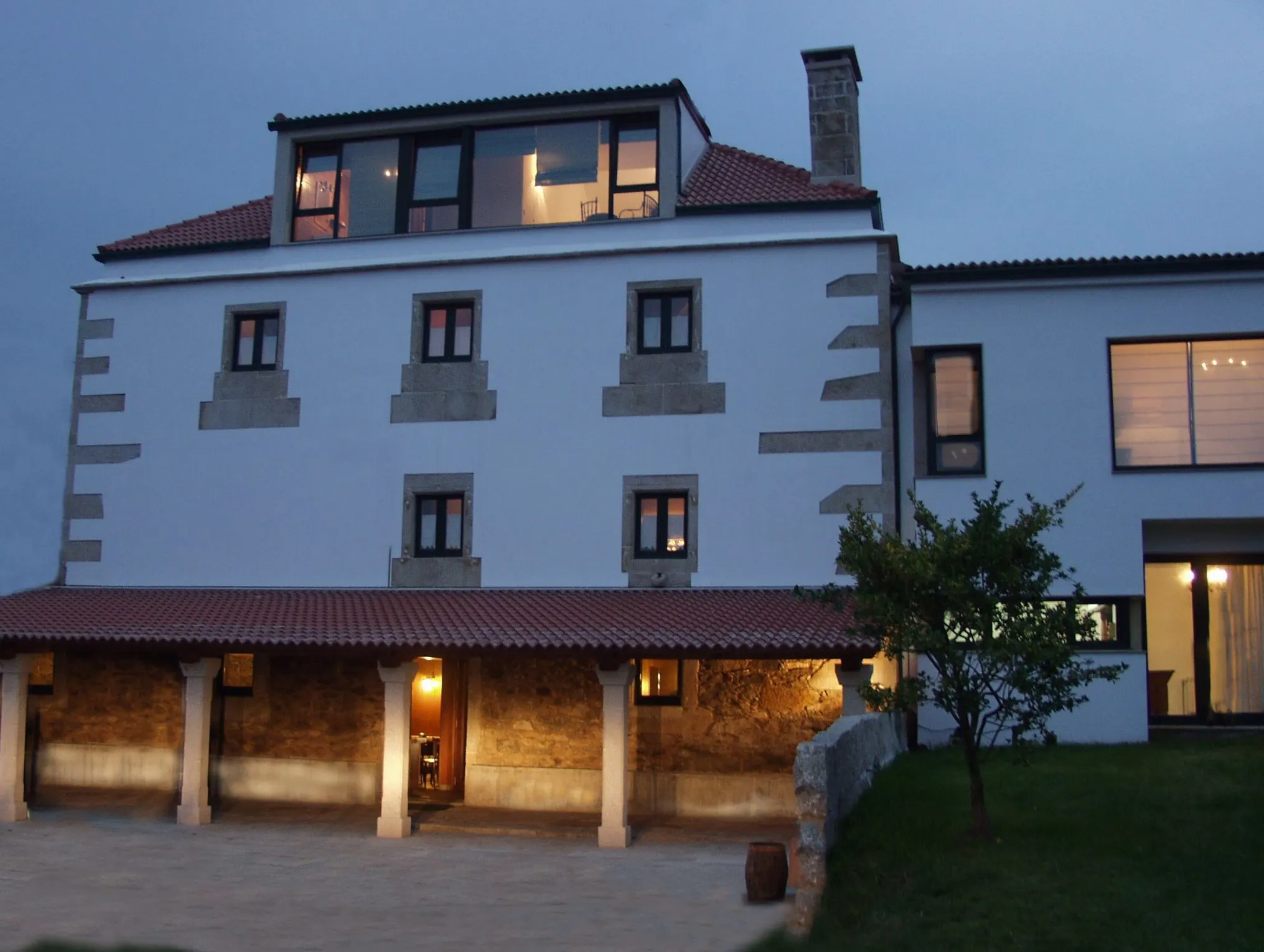 Fachada exterior de Casa do Vento en Baio (Zas), iluminada al atardecer, con porche cubierto y jardín.