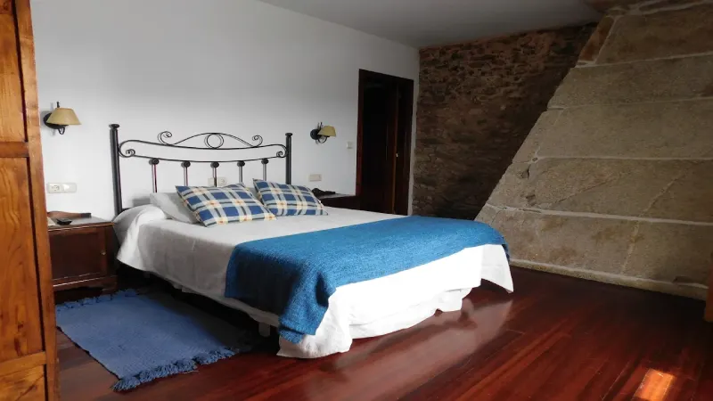 Habitación doble de Casa do Vento con cama de matrimonio, cabecero de forja, colcha azul y paredes de piedra.