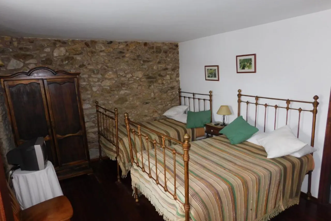 Habitación doble para dos personas en Casa do Vento, Baio (Zas), con dos camas individuales, cabeceros metálicos y pared de piedra.