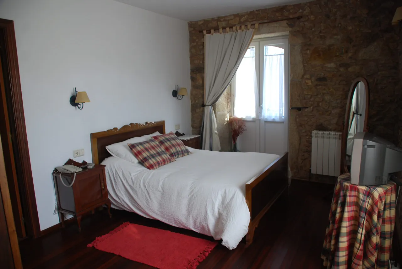 Habitación doble de uso individual para una persona en Casa do Vento, Baio (Zas), con cama de madera y paredes de piedra.