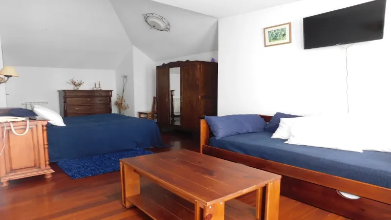 Habitación de Casa do Vento con dos camas, mobiliario de madera, televisión y zona de estar.