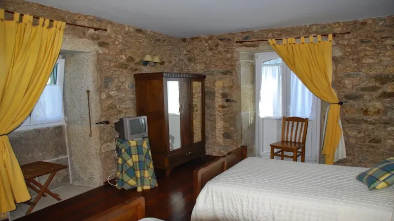 Habitación de Casa do Vento con paredes de piedra, cama de madera, armario tradicional y cortinas amarillas.