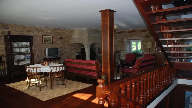 Salón común de Casa do Vento en Costa da Morte, con muebles de madera, sofás, chimenea y paredes de piedra.