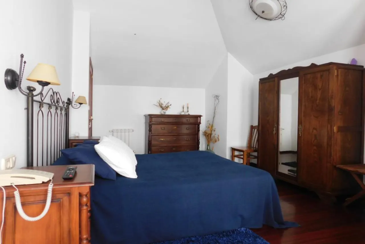 Suite para dos personas en Casa do Vento, Baio (Zas), con cama de matrimonio, cabecero de forja y mobiliario de madera.